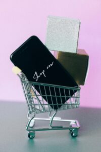 Mini shopping cart with smartphone and gift boxes, symbolizing online shopping.
